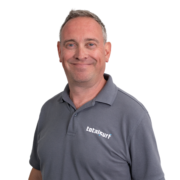 Man in a gray Totalsurf polo shirt standing against a plain white background, smiling slightly.