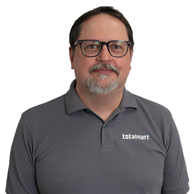 Man with glasses and goatee wearing a gray "totalsurf" polo shirt, facing the camera.