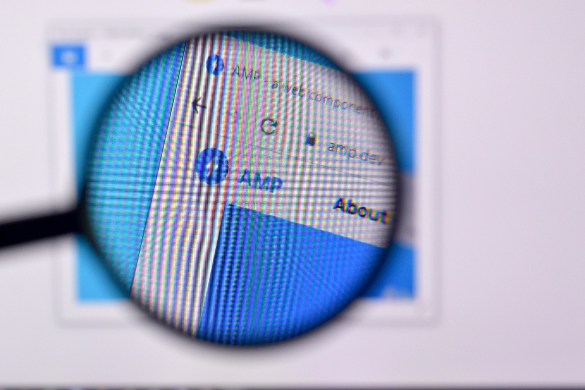 Computer screen showing the AMP website homepage magnified by a handheld magnifying glass.