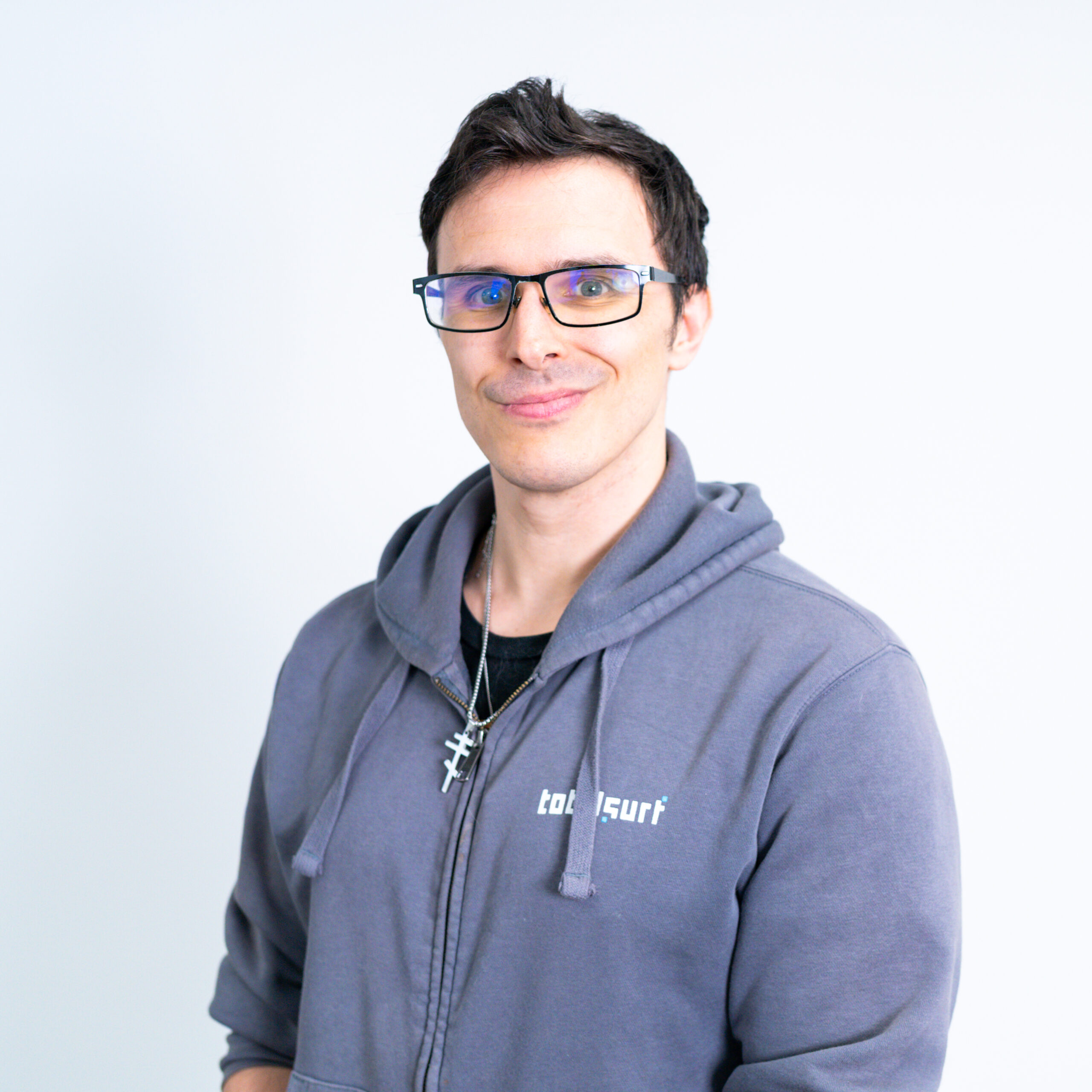 Person wearing glasses and a gray hoodie stands against a plain white background, facing the camera.
