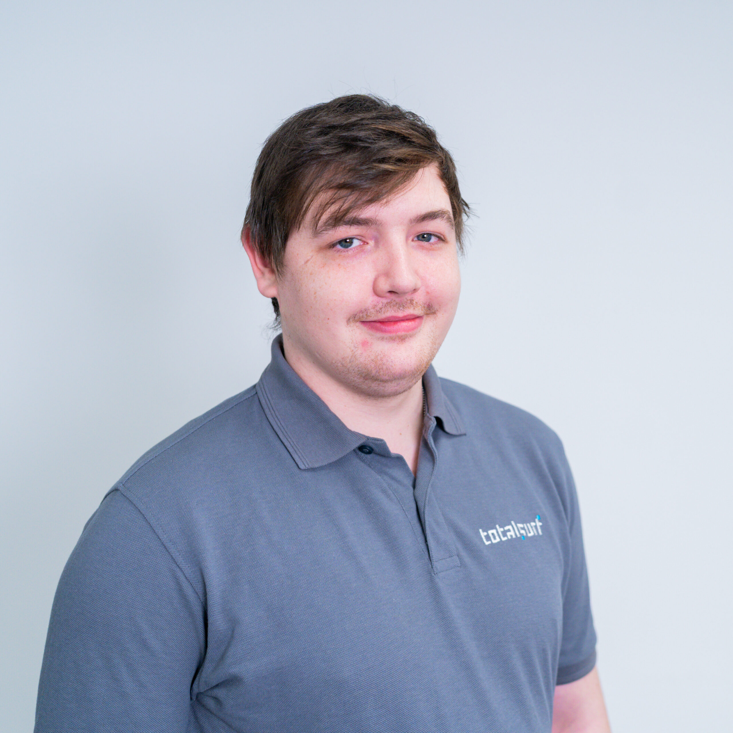 A man in a grey "totalsuit" polo shirt stands against a plain light background, facing forward.