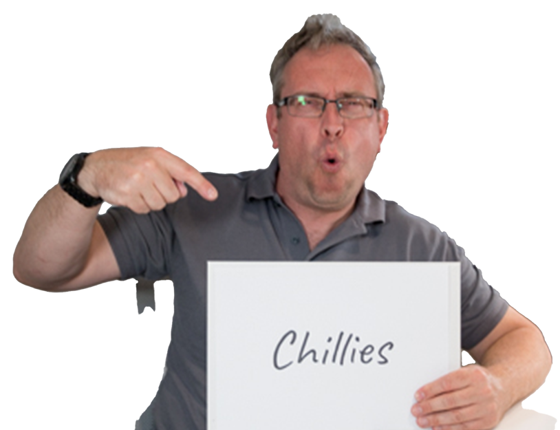Man in gray shirt points to a sign he is holding that says "Chillies" in handwritten text.