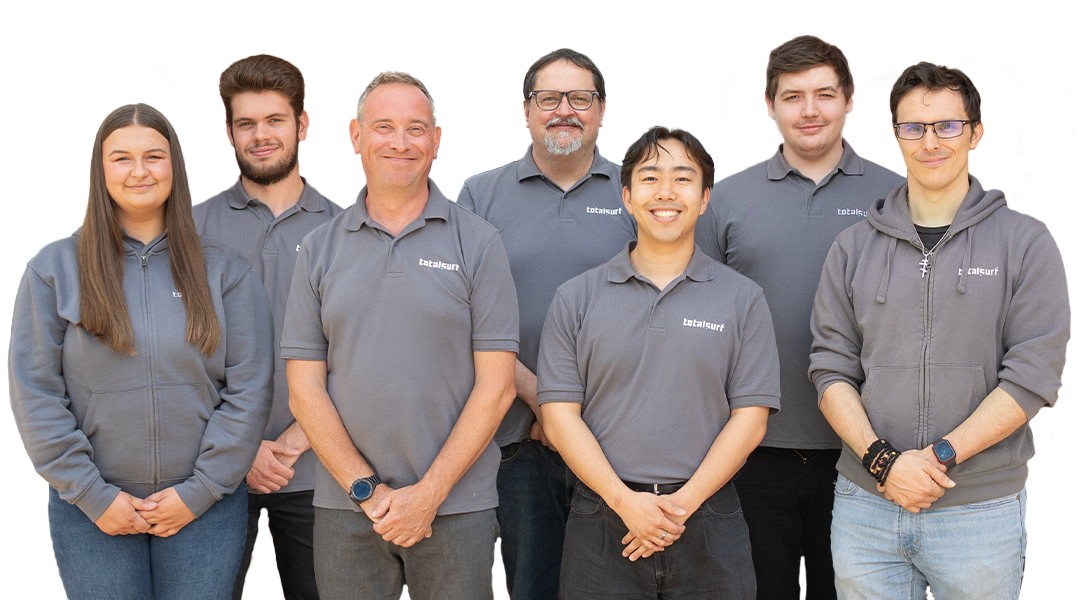 Seven people in matching gray tops stand in two rows against a plain light background, smiling.