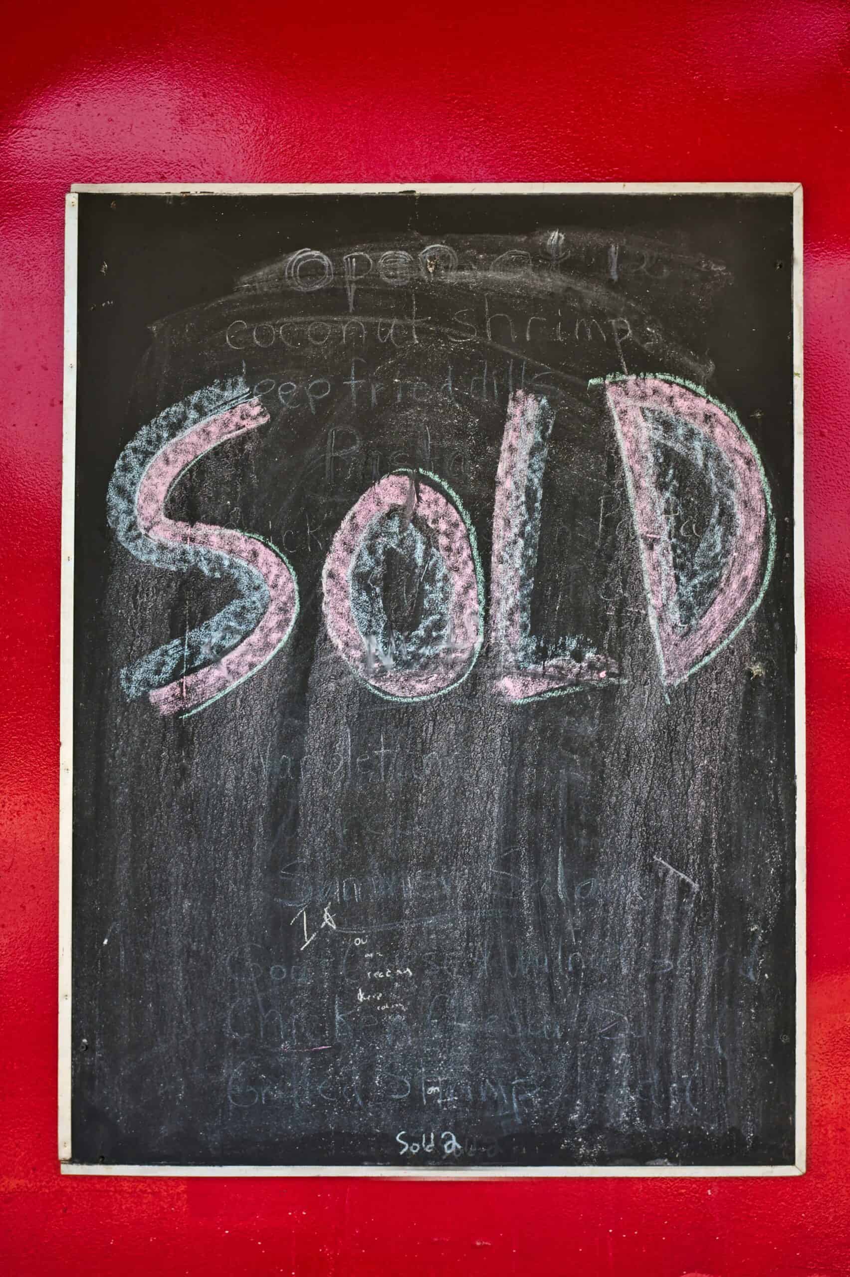 Chalkboard with the word "SOLD" written in large letters, hanging on a red wall.